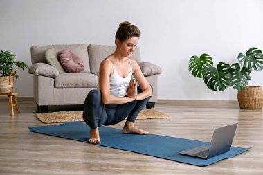 Spor yapan genç bir kadın kendi evinde yoga öğretiyor. Yogini 'nin canlı yayını, oturma odasındaki varyasyonları gösteriyor. İç arkaplan, kopyalama alanı, kapat.