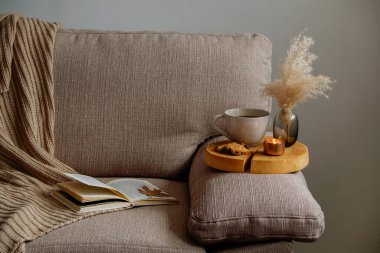 Kasım ruh hali konsepti. Kahverengi örgü süveter, açık kitap, büyük bardak çay ve kanepede çikolatalı kurabiyeler. Sonbahar sezonunda evde kalmak için sembolik nesneler. Kapat, kopyala boşluk, arkaplan