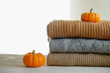 Bir sürü örülmüş sıcak pastel renkli süveter farklı örgü desenleri yığılmış, görünür doku. Şık bir sonbahar kış örgü elbisesi ve üstünde de balkabağı. Kapat, metin için boşluk kopyala.