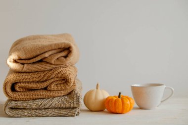Bir sürü örülmüş sıcak pastel renkli süveter farklı örgü desenleri yığılmış, görünür doku. Şık bir sonbahar kış örgü elbisesi ve üstünde de balkabağı. Kapat, metin için boşluk kopyala.