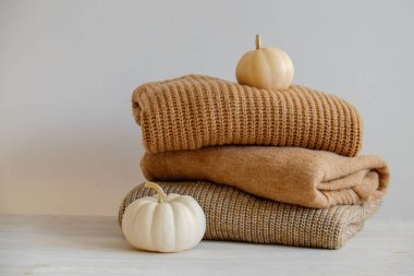 Bir sürü örülmüş sıcak pastel renkli süveter farklı örgü desenleri yığılmış, görünür doku. Şık bir sonbahar kış örgü elbisesi ve üstünde de balkabağı. Kapat, metin için boşluk kopyala.