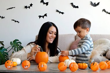 Üç yaşındaki oğluyla birlikte evde cadılar bayramı için dekorasyon hazırlıyorlardı. Kadın çocuğuyla güzel vakit geçiriyor, balkabağı oyuyor. Kapat, kopyala boşluk, arkaplan.