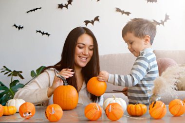 Üç yaşındaki oğluyla birlikte evde cadılar bayramı için dekorasyon hazırlıyorlardı. Kadın çocuğuyla güzel vakit geçiriyor, balkabağı oyuyor. Kapat, kopyala boşluk, arkaplan.