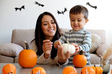 Üç yaşındaki oğluyla birlikte evde cadılar bayramı için dekorasyon hazırlıyorlardı. Kadın çocuğuyla güzel vakit geçiriyor, balkabağı oyuyor. Kapat, kopyala boşluk, arkaplan.