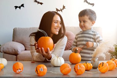 Üç yaşındaki oğluyla birlikte evde cadılar bayramı için dekorasyon hazırlıyorlardı. Kadın çocuğuyla güzel vakit geçiriyor, balkabağı oyuyor. Kapat, kopyala boşluk, arkaplan.