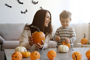 Üç yaşındaki oğluyla birlikte evde cadılar bayramı için dekorasyon hazırlıyorlardı. Kadın çocuğuyla güzel vakit geçiriyor, balkabağı oyuyor. Kapat, kopyala boşluk, arkaplan.
