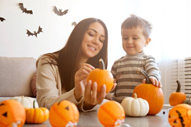 Üç yaşındaki oğluyla birlikte evde cadılar bayramı için dekorasyon hazırlıyorlardı. Kadın çocuğuyla güzel vakit geçiriyor, balkabağı oyuyor. Kapat, kopyala boşluk, arkaplan.