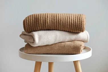 Beyaz ahşap masa üzerine yığılmış farklı örgü desenleri olan bir grup sıcak pastel renkli süveter, beyaz duvar arka planı. Sonbahar mevsimi örgü. Kapat, boşluğu kopyala.