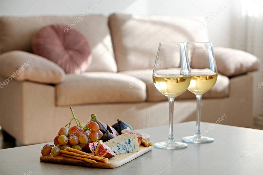 Two wineglasses of vintage chardonnay with delicious appetizers. Couple of glasses of white wine, italian breadsticks, figs and grapes. Interior background. Close up, copy space.