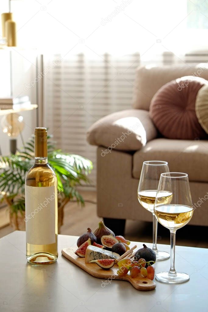 Bottle of a vintage chardonnay with two poured glasses, figs, grapes, blue cheese and grissini breadsticks. Copy space, top view, flat lay, close up, background.