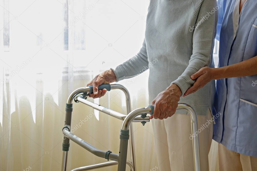 Cropped shot of an elderly woman in nursing home room holding walking frame with wrinkled hand. Senior lady grabbing metal walker's handles. Interior background, copy space, close up.