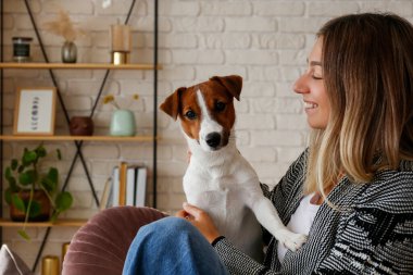 Kanepede sevimli Jack Russell Terrier köpeği ile oynayan genç ve güzel hippi kadının portresi. Köpeğiyle eğlenen bir kız. Arkaplan, kapat, boşluğu kopyala