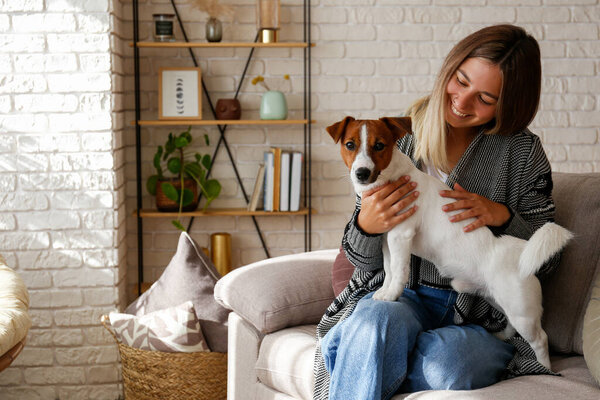 Portrait of young beautiful hipster woman playing with her adorable jack russell terrier puppy on the couch. Loving girl with her dog having fun. Background, close up, copy space