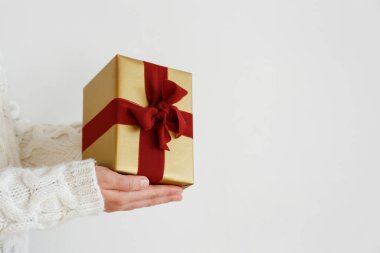 Beyaz örgü süveter giyen, ipek bir fiyonkla bağlanmış, kırmızı arka planda bağlı bir kadın. Bir kadının elinde Noel hediyesi. Kapat, metin için boşluk kopyala.