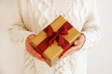 Beyaz örgü süveter giyen, ipek bir fiyonkla bağlanmış, kırmızı arka planda bağlı bir kadın. Bir kadının elinde Noel hediyesi. Kapat, metin için boşluk kopyala.