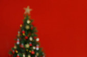 Rozmazané zdobené vánoční stromeček v měkkých žlutých světlech s bokeh efekt na izolovaném červeném pozadí. Zavřít, kopírovat mezeru.