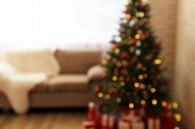 Geleneksel Noel çam ağacını Noel süslemeleriyle bulanıklaştırdı. Dekoratif ışıklar köknar üzerinde bokeh efektiyle parlıyor. Kapat, bej koltuklu iç arkaplan, metin için kopyalama alanı.