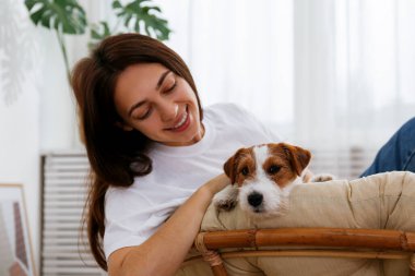 Papasan sandalyesinde güzel bir kadının portresi. Tel saçlı Jack Russel terrier köpeği. Sert kaplamalı sevimli kız eğleniyor. Arkaplan, kapat, boşluğu kopyala.