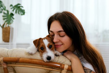 Papasan sandalyesinde güzel bir kadının portresi. Tel saçlı Jack Russel terrier köpeği. Sert kaplamalı sevimli kız eğleniyor. Arkaplan, kapat, boşluğu kopyala.