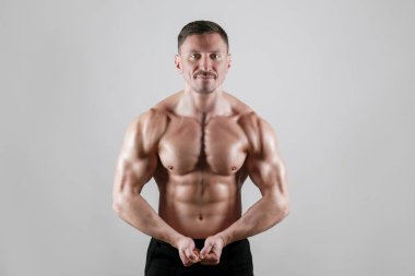 İzole edilmiş beyaz arka planda poz veren profesyonel vücut geliştirici. Spor salonundaki antrenörün kaslarını esnetirkenki görüntüsü. Kapat, boşluğu kopyala.