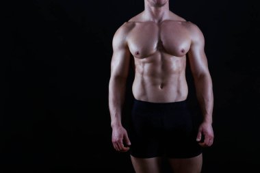 Tecrit edilmiş siyah arka planda poz veren profesyonel vücut geliştirici. Spor salonundaki antrenörün kaslarını esnetirkenki görüntüsü. Kapat, boşluğu kopyala.