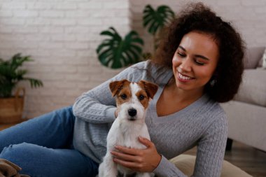 Portrait of young beautiful black woman with her adorable wire haired Jack Russel terrier puppy at home. Loving girl with rough coated pup having fun on the couch. Background, close up, copy space.