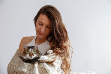 Yeşil gözlü şirin Sibirya kedisi tutan genç bir kadının portresi. Kadın uzun saçlı kediciğine sarılıyor. Arka plan, kopyalama alanı, kapatın. Tapılası evcil hayvan konsepti.