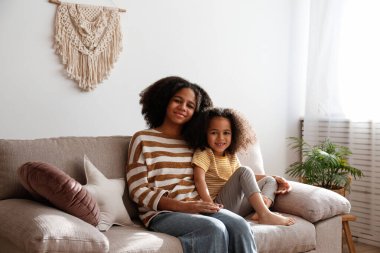 Küçük ve büyük kız kardeş evde birlikte vakit geçiriyorlar. Farklı yaşlarda iki siyah kız kucaklaşıp sevgi gösteriyorlar. Siyahi dişi kardeşler eğleniyor ve kaynaşıyorlar. Arkaplan, kopyala boşluk, kapat.