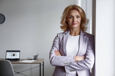 Güzel sarışın iş kadını, kollarını göğsünde kavuşturarak duvara yaslanıyor. Eflatun ceketli, katlanmış elleri olan kendine güvenen yetişkin bir kadın. Ofis arkaplanı, kopyalama alanı, kapat