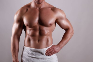 Profesyonel vücut geliştirici, gri arka planda sadece havluyla poz veriyor. Stüdyoda kaslarını esneten formasız bir adamın fotoğrafı. Kapat, boşluğu kopyala.