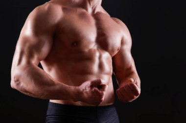 Tecrit edilmiş siyah arka planda poz veren profesyonel vücut geliştirici. Spor salonundaki antrenörün kaslarını esnetirkenki görüntüsü. Kapat, boşluğu kopyala.