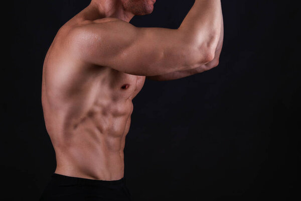 Professional bodybuilder posing over isolated black background. Front Double Biceps pose. Studio shot of a fitness trainer flexing the muscles. Close up, copy space.
