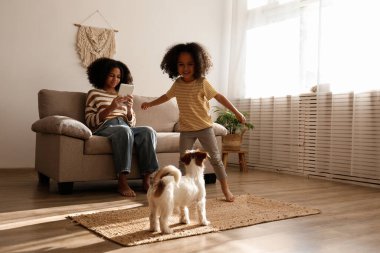 Farklı yaşlarda iki güzel siyah kız sevimli tel saçlı Jack Russel teriyerleriyle evde oynuyorlar. Sert kaplamalı sevimli kız kardeşler eğleniyor. Arkaplan, kapat, boşluğu kopyala.