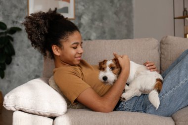 Genç ve güzel bir kızın portresi. Tel saçlı Jack Russel teriyeri köpeğiyle evde. Kanepede oturan sert kaplamalı bir genç. İç arkaplan, kapat, kopyala