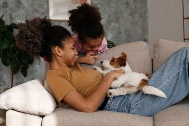 Farklı yaşlarda iki güzel siyah kız sevimli tel saçlı Jack Russel teriyerleriyle evde oynuyorlar. Sert kaplamalı sevimli kız kardeşler eğleniyor. Arkaplan, kapat, boşluğu kopyala.