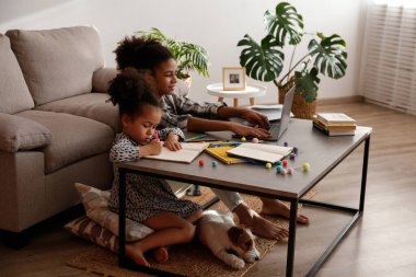 Farklı iki güzel siyah kız ve tapılası tel saçlı Jack Russel Terrier köpekleri evde dizüstü bilgisayar kullanıyorlar. Sert kaplamalı sevimli kız kardeşler eğleniyor. Arkaplan, kapat, boşluğu kopyala.