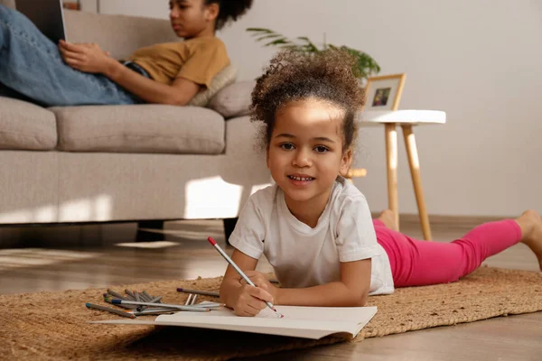 İki güzel siyah kız kardeş evlerinde farklı aktivitelerde bulundular. Sevgili kız kardeşler birlikte vakit geçiriyorlar, dizüstü bilgisayarın yanında ve çizim defterinde daha küçük çizimler yapıyorlar. Arkaplan, kapat, boşluğu kopyala.
