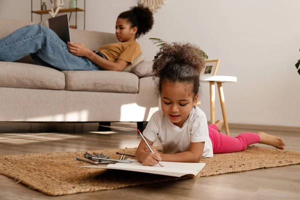 İki güzel siyah kız kardeş evlerinde farklı aktivitelerde bulundular. Sevgili kız kardeşler birlikte vakit geçiriyorlar, dizüstü bilgisayarın yanında ve çizim defterinde daha küçük çizimler yapıyorlar. Arkaplan, kapat, boşluğu kopyala.