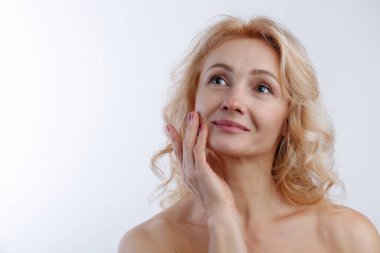 Temiz tenli, tenli, izole beyaz arka planda yüzüne dokunan şehvetli yetişkin bir kadının stüdyo portresi. Orta yaşlı, dalgalı sarı saçlı, çıplak omuzlu bir kadın. Kapat, boşluğu kopyala.