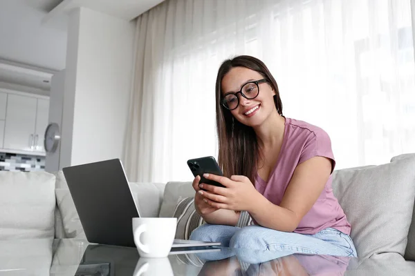 Gözlüklü Esmer Bir Kadının Portresi Evde Oturuyor Dizüstü Bilgisayarla Telefonu — Stok fotoğraf
