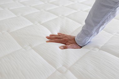 Cropped shot of man testing white orthopedic matress on firmness. Male pressing hypoallergenic foam mattresses surface to check its softness. Close up, copy space, top view, background. clipart