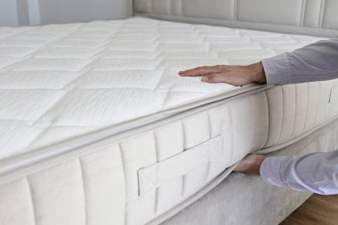 Cropped shot of man testing white orthopedic matress on firmness. Male pressing hypoallergenic foam mattresses surface to check its softness. Close up, copy space, top view, background. clipart