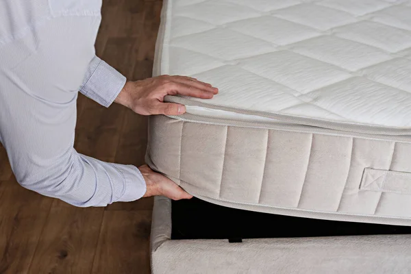 New bed delivery and assembly service concept. Cropped shot of male worker\'s hands in process of laying the orthopedic foam mattress on carcass in customer\'s bedroom. Close up, copy space, background.