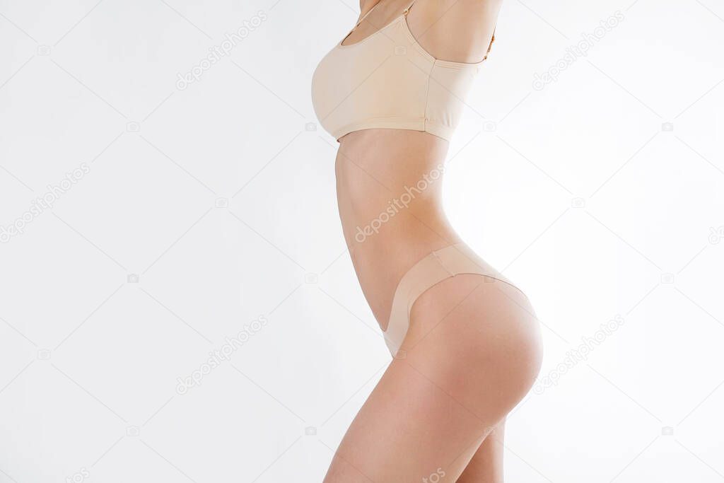 Unrecognizable fit woman in lingerie standing with hands up isolated on white background. Torso of slim attractive female with flat belly in beige underwear. Copy space, close up, cropped shot.