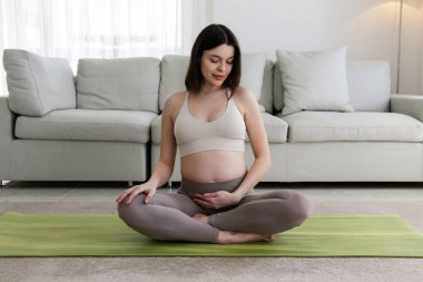 Hamileliğin ikinci üç ayında yoga yapan güzel bir kadın. Lotus pozu verip meditasyon yapan hamile bir kadına yakın çekim. Sağlıklı hamilelik kavramı. Arkaplan, boşluğu kopyala.