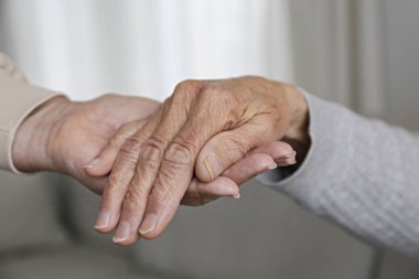 Yaşlı bakım evindeki olgun bir kadın hastane personeli hemşiresinden yardım alıyor. Yaşlanmış cilt ve bakım yapan yaşlı bir kadının ellerinin kırpılmış görüntüsü. Arkaplan, kopyala boşluk, kapat.