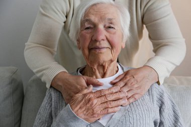 Unrecognizable female expressing care towards an elderly lady, hugging her from behind holding hands. Two adult women of different age. Family values concept. lose up, copy space, background.