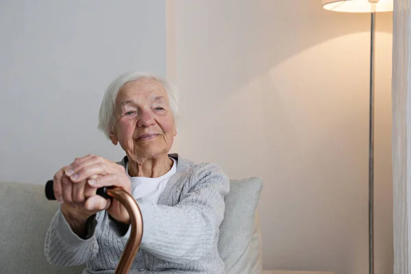 Retrato Uma Mulher Sênior Sentada Sofá Casa Apoiada Uma Bengala — Fotografia de Stock