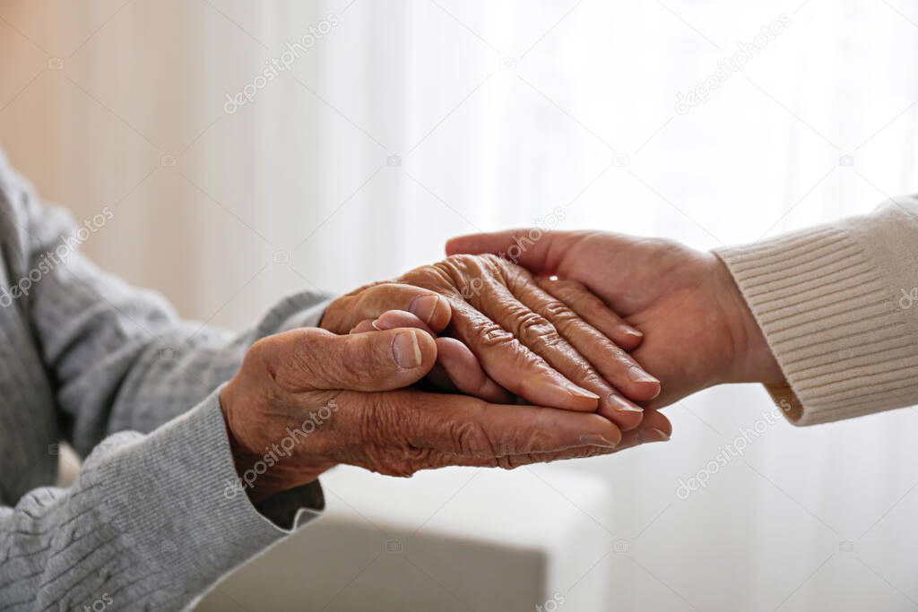 Mature female in elderly care facility gets help from hospital personnel nurse. Cropped shot of senior woman's hands with aged wrinkled skin and care giver. Background, copy space, close up.