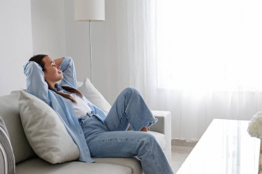 Uzun düz esmer saçlı güzel bir kadının portresi kanepede oturuyor, rahatlıyor ve yalnız zamanının tadını çıkarıyor. Kahverengi gözlü kadın rahat bir pozisyonda. Boşluğu, arkaplanı kopyala, kapat